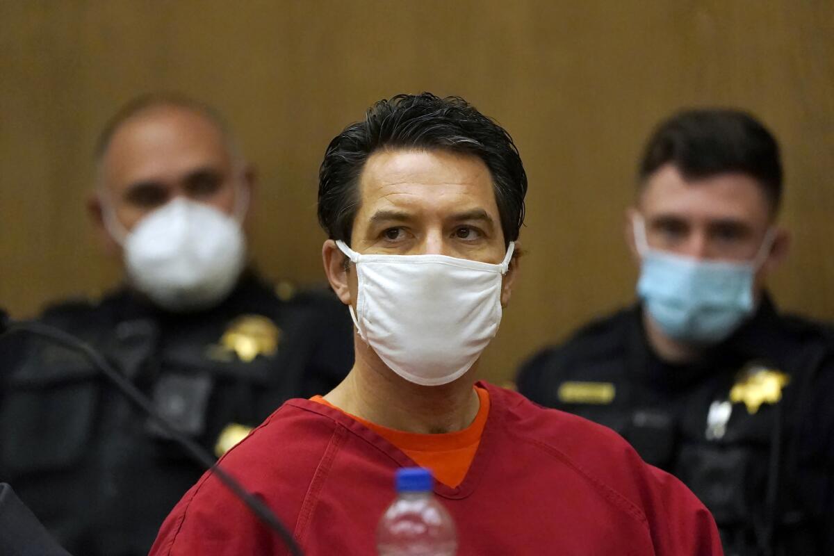 A man in a prison jumpsuit wears a mask in court.