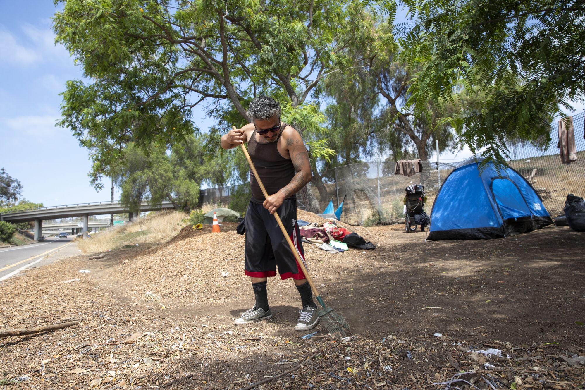 Luis Medina, 44, rakes the area outside of his tent along the freeway on Friday.