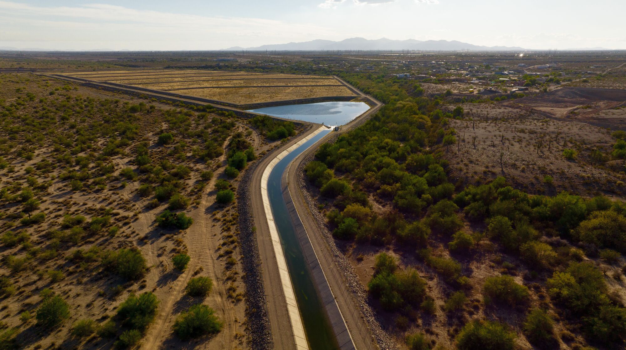 a canal surrounded by shrubs runs into a basin 