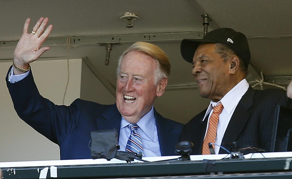 Dodgers announcer Vin Scully waves to fans while standing next to former Giants great Willie Mays in the booth
