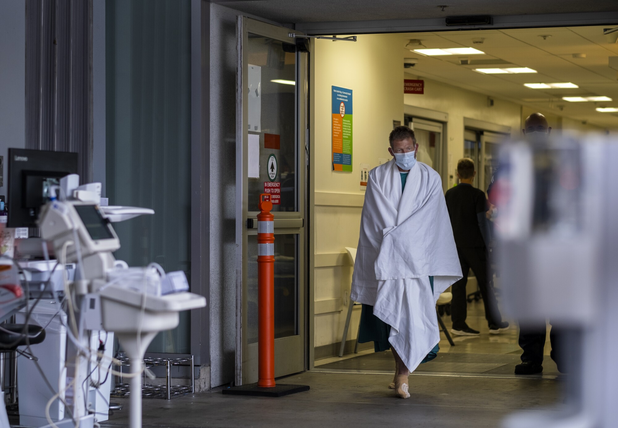 A masked patient wrapped in a blanket walks at MLK Community Hospital.