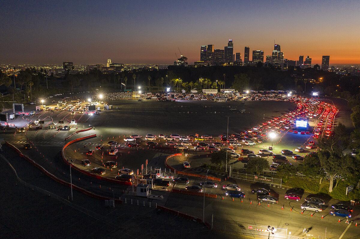 Long lines of vehicles snake through the parking lot of Dodger Stadium at night with the L.A. skyline in the background