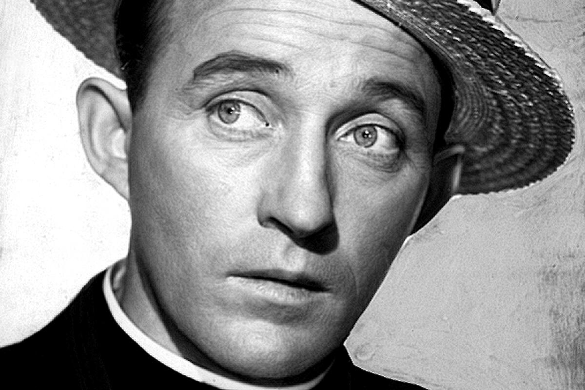 A black-and-white movie still shows a man in closeup wearing a hat and a priest's collar