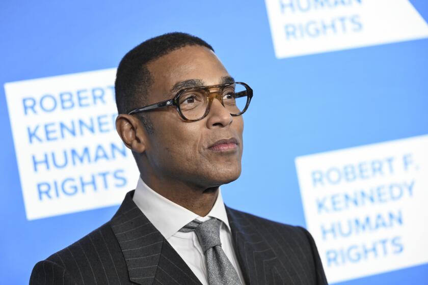 Man, don lemon, looking toward right, wearing thick-rimmed glasses and black suit with gray tie