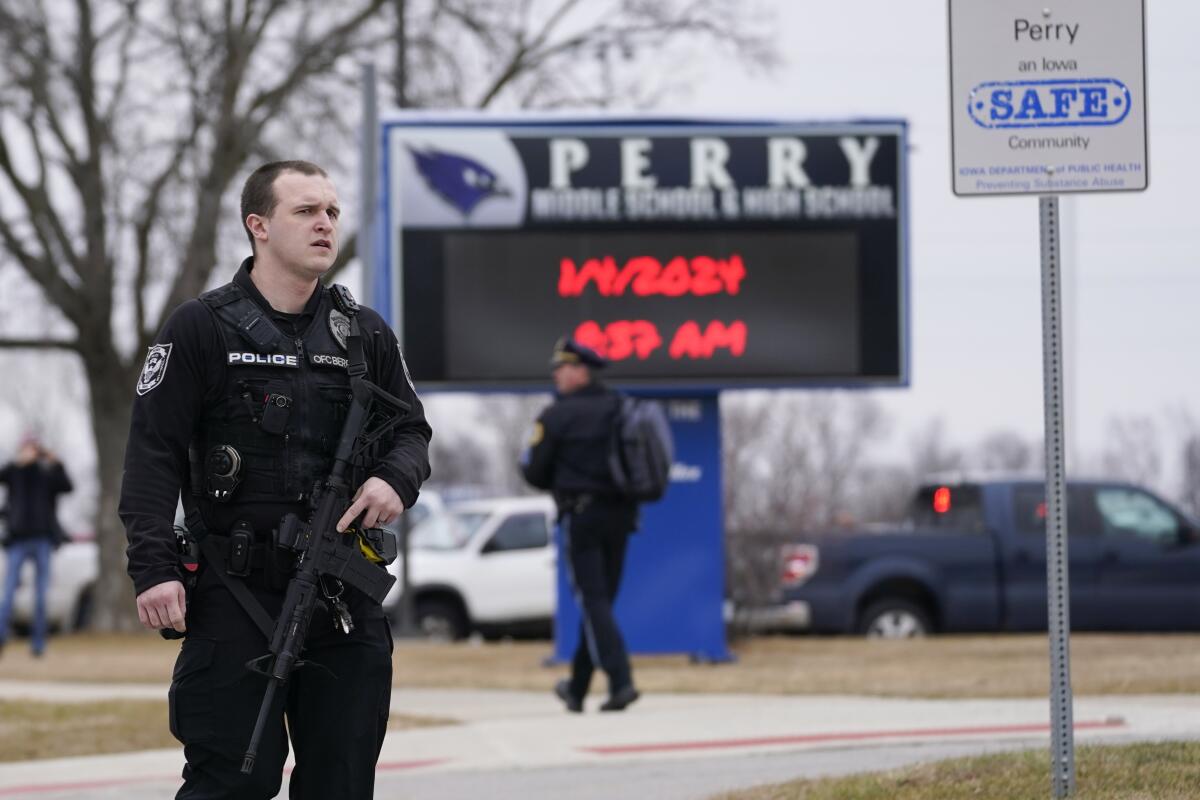 A police officer with a gun stands near a sign for Perry Middle School and High School 