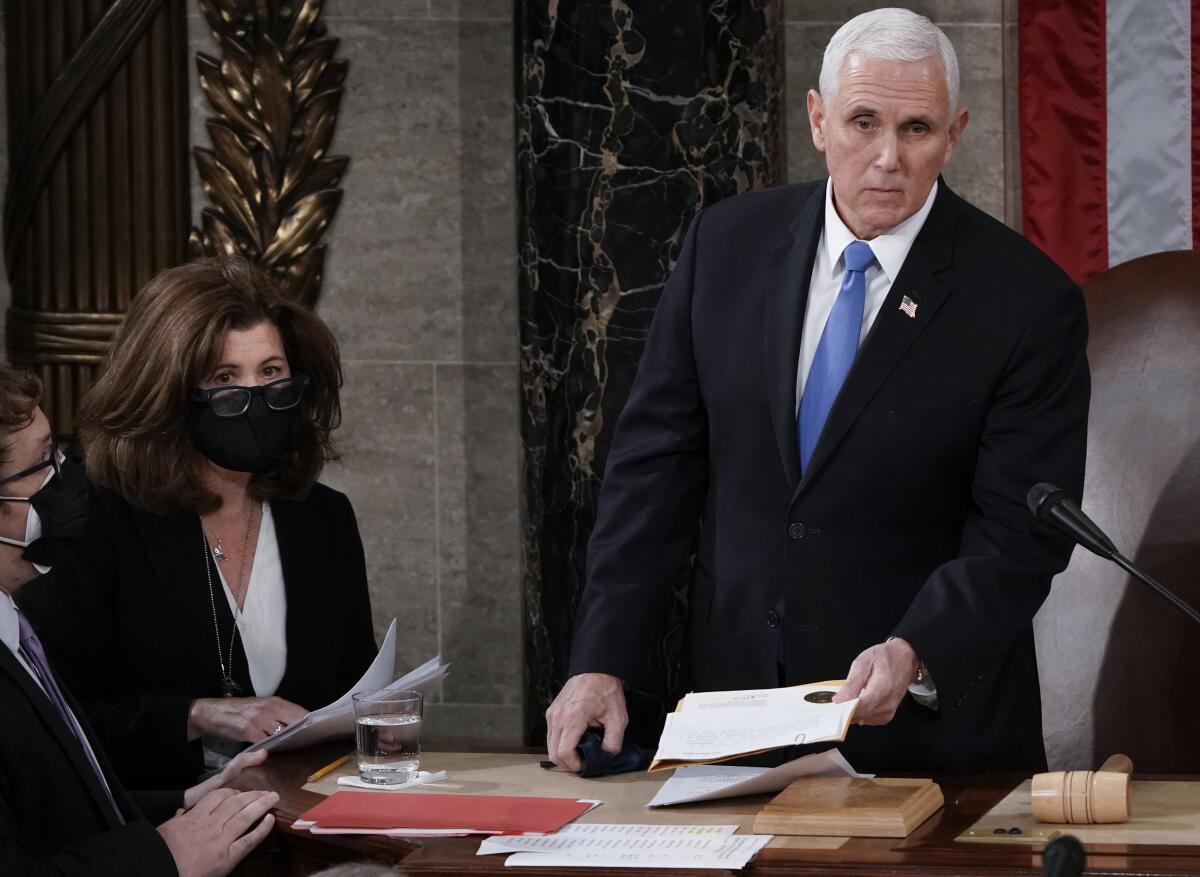 A woman, left, in a face mask, and a man, both in business attire