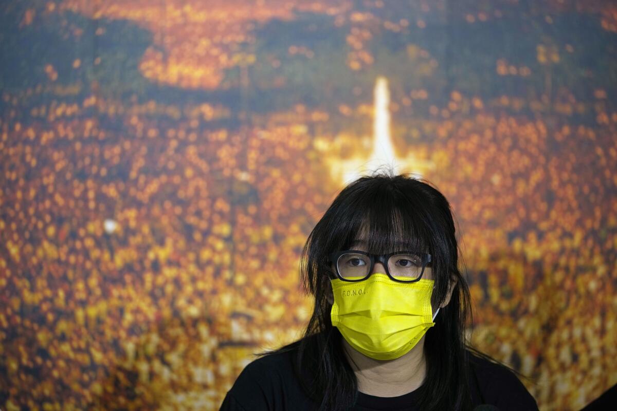 A woman in a yellow face mask sits in front of a colorful picture.