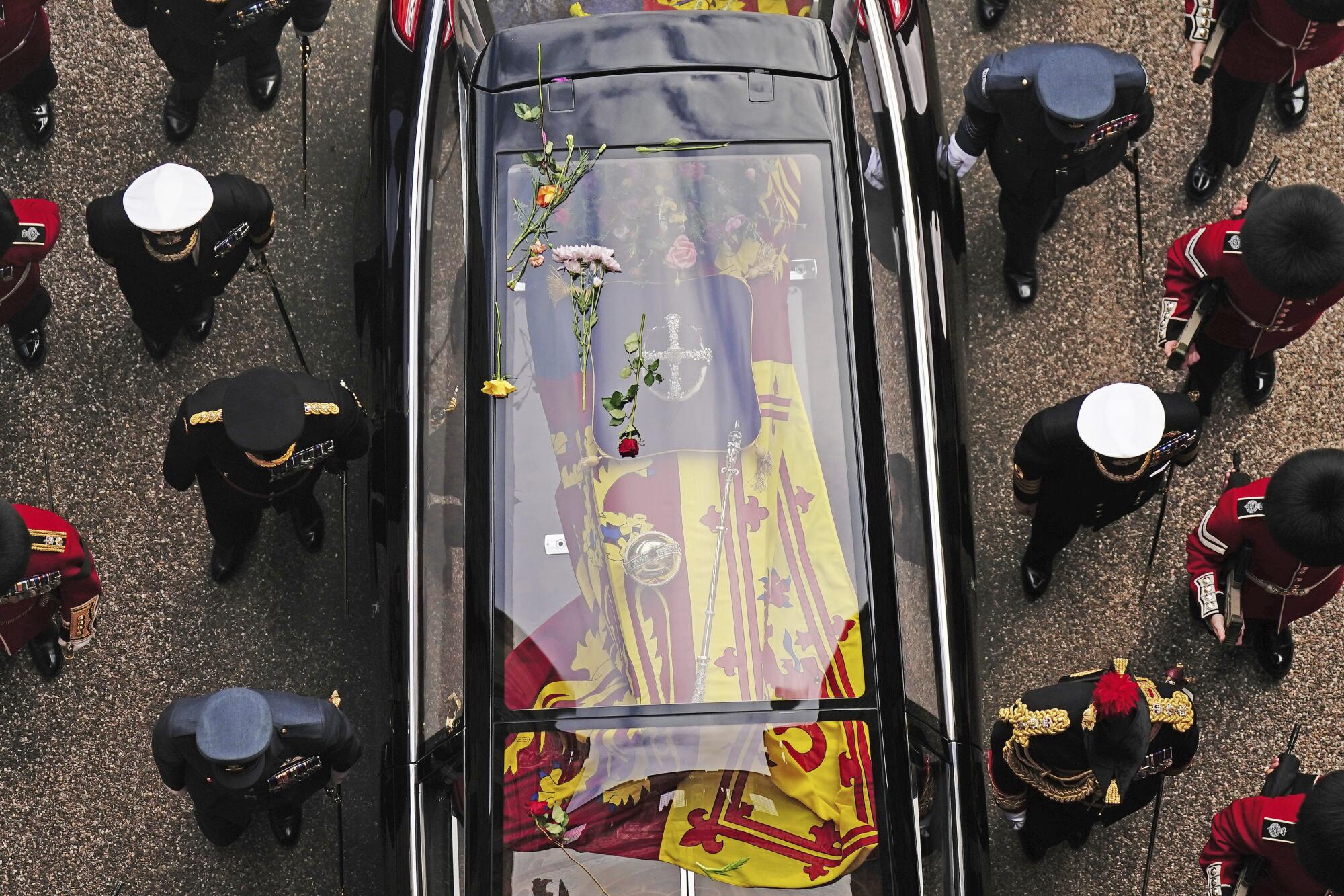 Flowers on the glass-roofed hearse carrying the coffin of Queen Elizabeth II with uniformed people flanking it