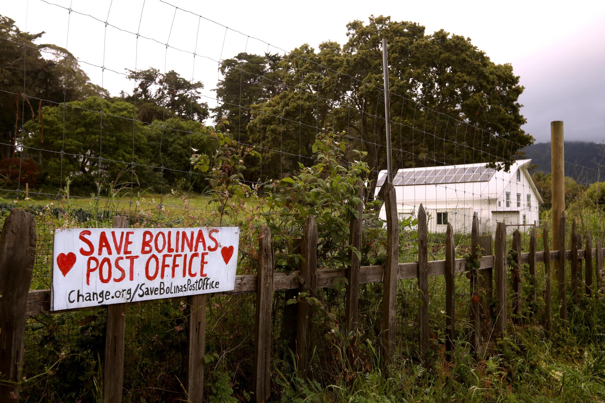 A hand-painted sign tacked to a picket fence calls for saving the Bolinas post office.