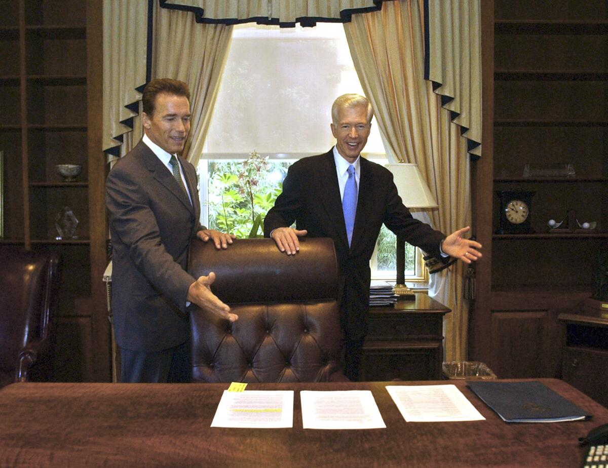 Gov.-elect Arnold Schwarzenegger and Gov. Gray Davis joke with each other in an ornate office.