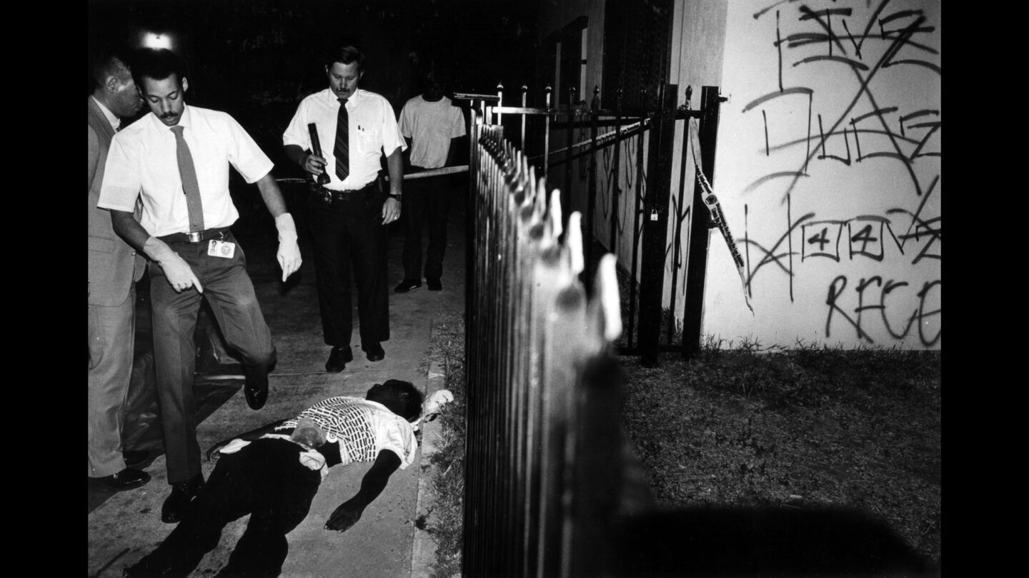 A coroner's team prepares to examine the body of a gang member killed in a drive-by shooting on 42nd Place. Five Deuce Hoover Crips graffiti can be seen crossed out on the wall of the apartment next door.