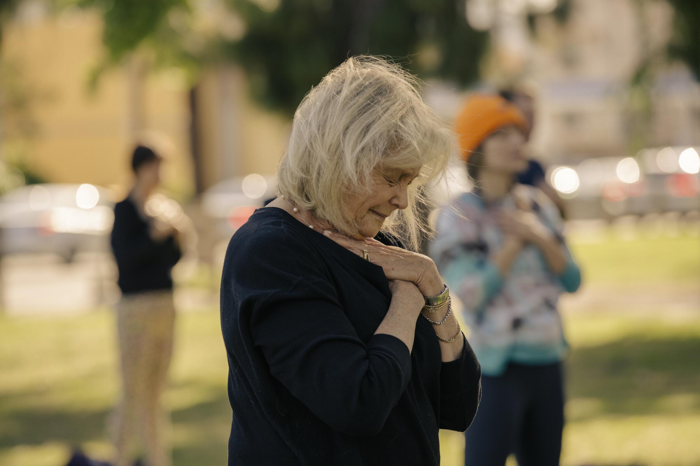 A woman stands outside with her hands crossed over her heart.