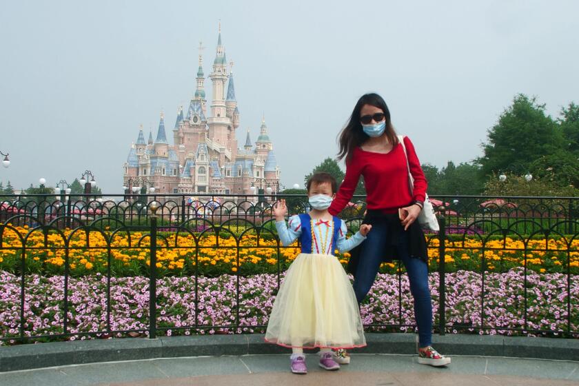A young visitor, wearing face masks, waves at the Disneyland theme park in Shanghai as it reopened after the coronavirus closure, Monday, May 11, 2020. Visits will be limited initially and must be booked in advance, and the company said it will increase cleaning and require social distancing in lines for the various attractions.(AP Photo/Sam McNeil)