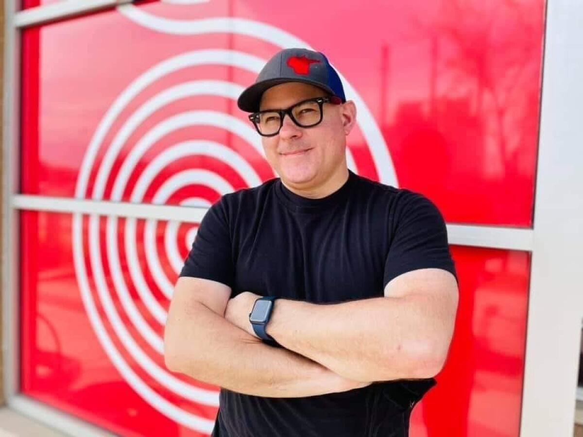 A man stands with arms folded in front of a window painted red with a white spiral design