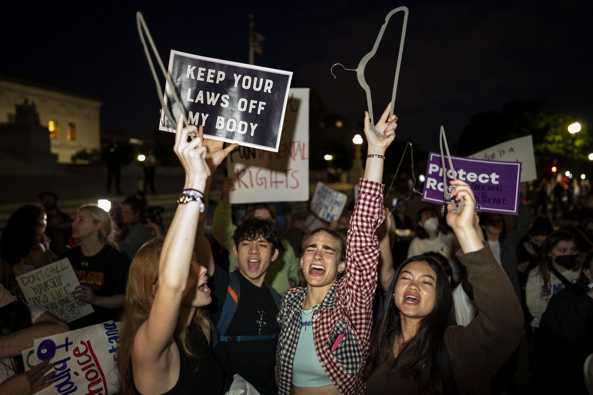 Abortion rights demonstrators chanting and holding up hangers and signs in the dark.