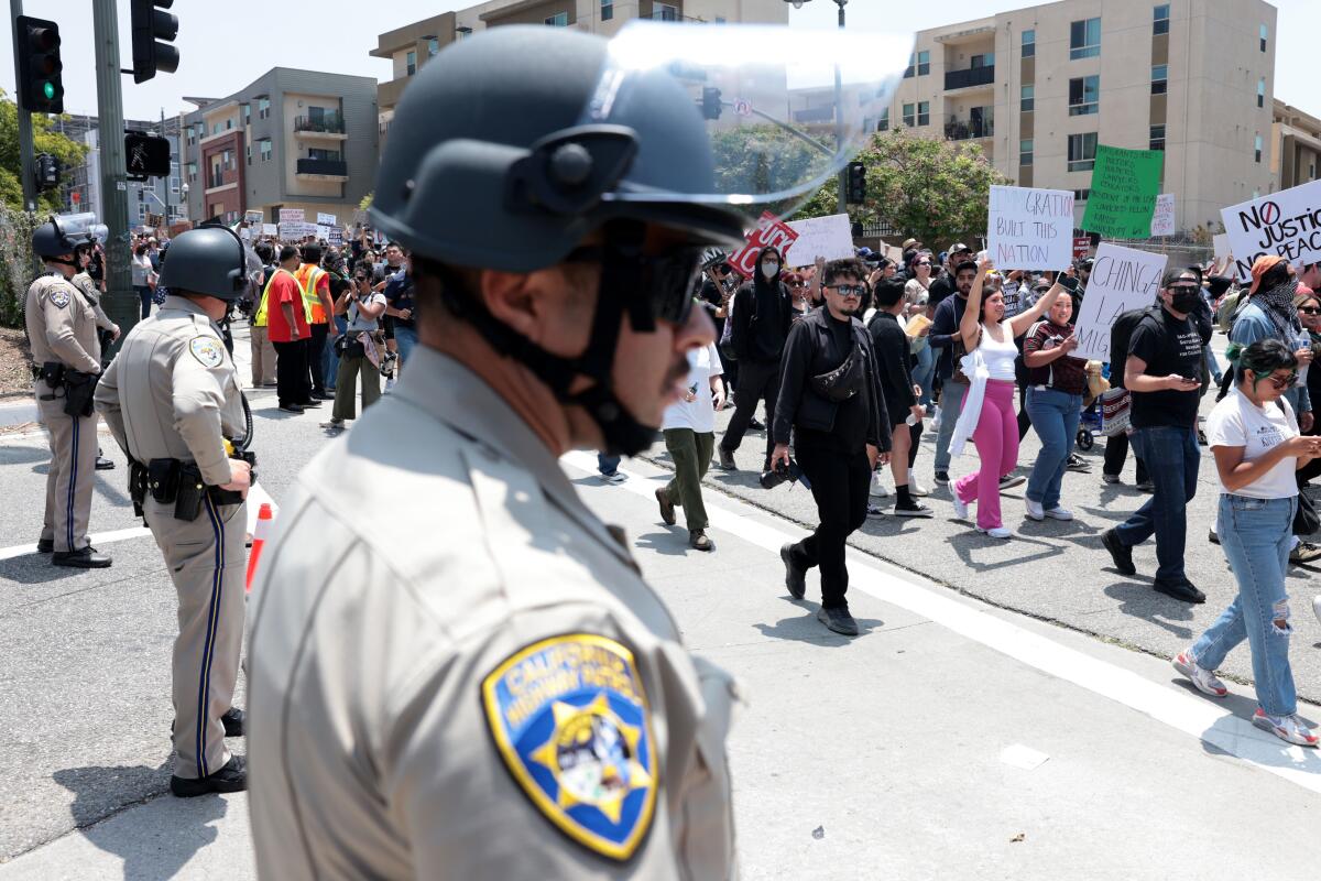 Police officers in riot helmets watch a procession of demonstrators.