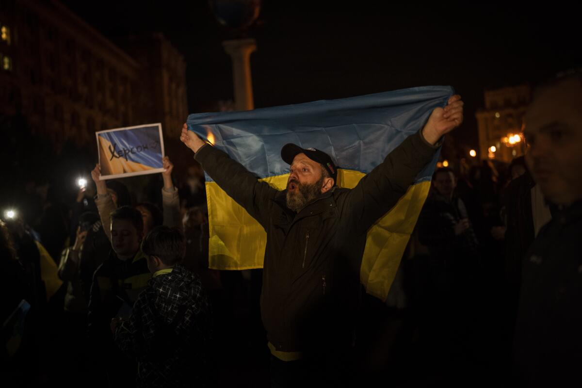 Ukrainians hold up the state flag outside in the dark.