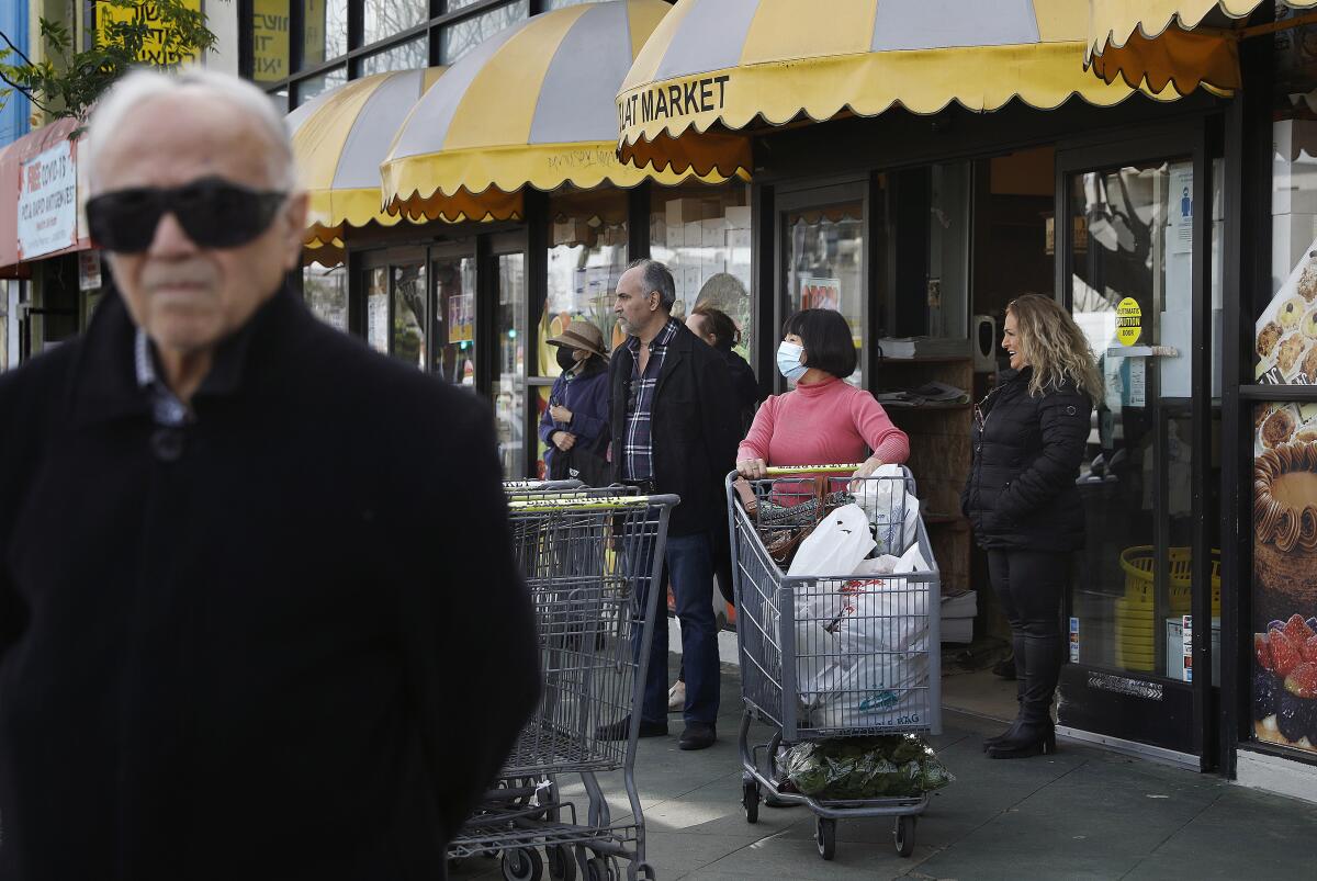 A small group of people stands with shopping carts outside of a store looking to the left of the frame.