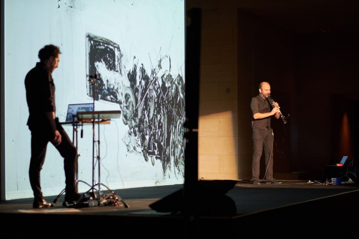Silkroad Ensemble clarinetist Kinan Azmeh performs while artist Kevork Mourad (left) creates live art on a screen behind him.