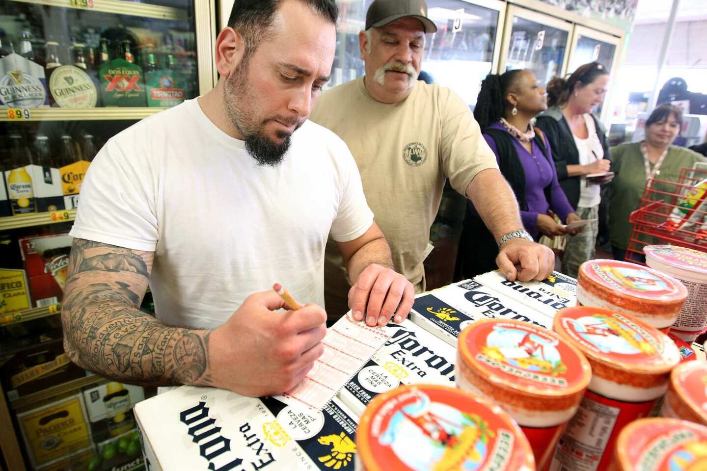 Josh DiLeva, left, picks numbers as Matte Jurevich, second from left, looks on while waiting in line to play the lottery at Mr. C's Liquor in San Pedro.