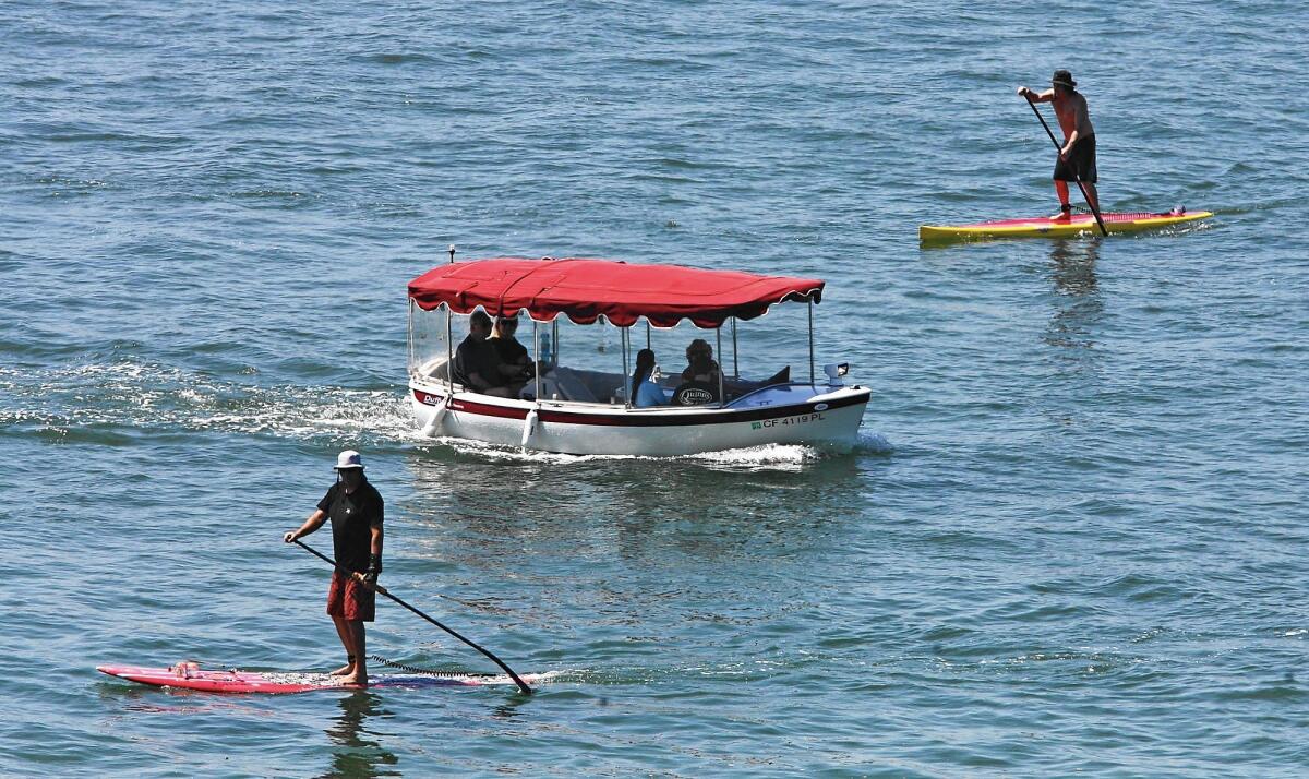 A boat moves between two stand–up paddleboarders at Newport Harbor. A city committee is looking into paddleboard use in the harbor and whether board rental companies properly educate their customers about safely navigating the waterways.