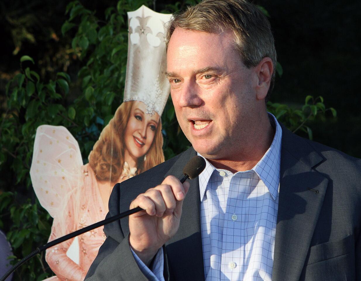 Mayor Pro Tem Jon Curtis, with the Good Witch of the North peaking over his shoulder, talks to the crowd at Olberz Park in La Cañada at the annual La Cañada Flintridge Chamber of Commerce mixer on Thursday, September 17, 2015.
