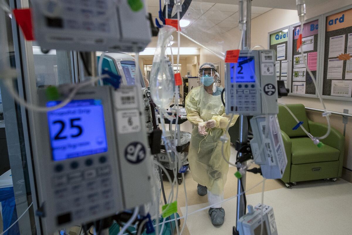 A masked and sheathed medical provider walks toward standing monitors.