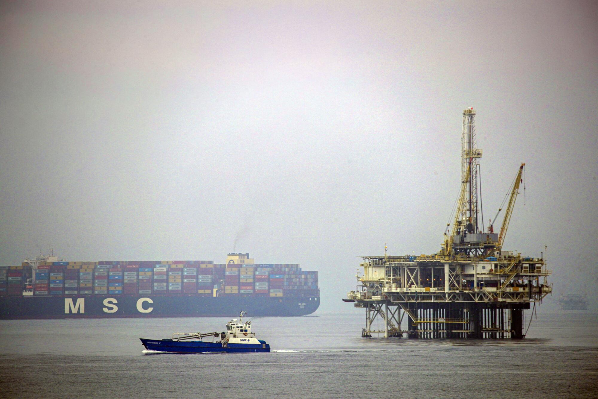 A cargo ship, an oil platform and a smaller boat on an overcast day.