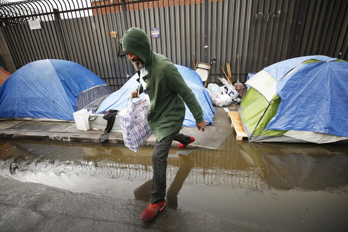 John Gunn leaps over the water at his tent in Skid Row where his belongings were soaked as rain and hail fall in downtown Los Angeles, Wednesday.