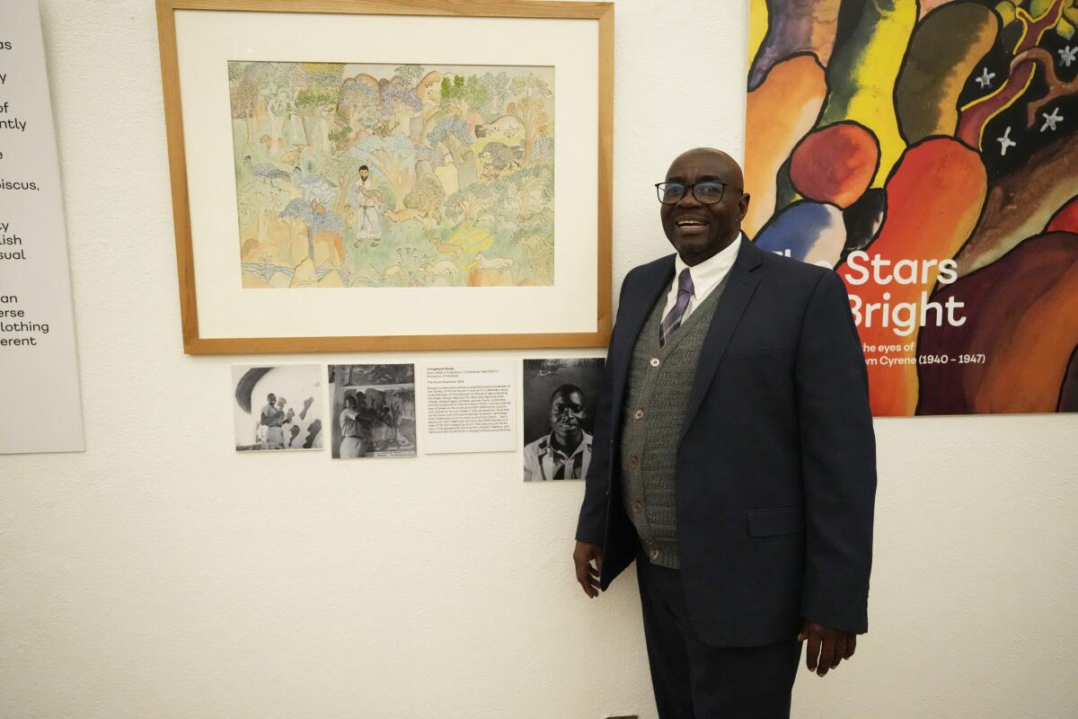 Gift Livingtsone Sango, 65, stands next to a painting by his father depicting Jesus as a Black man at the National Gallery of Zimbabwe, Thursday, July 14, 2022. The painting done by his late father in the 1940s is part of a historic exhibit, "The Stars are Bright," now showing in Zimbabwe for the first time since the collection left the country more than 70 years ago. A photograph of Sango's father, Livingstone, as a young boy hangs next to the painting. (AP Photo/Tsvangirayi Mukwazhi)