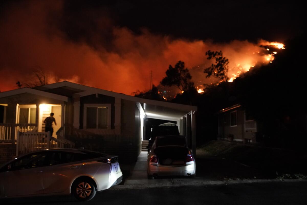Person entering a house in Sylmar as a wildfire blazes in the hills behind it