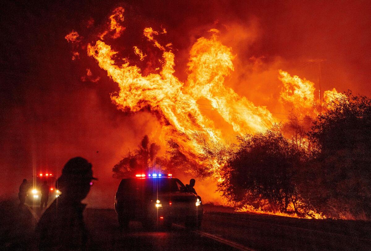 A law enforcement officer watches flames launch into the air from the Bear fire in Oroville, Calif.