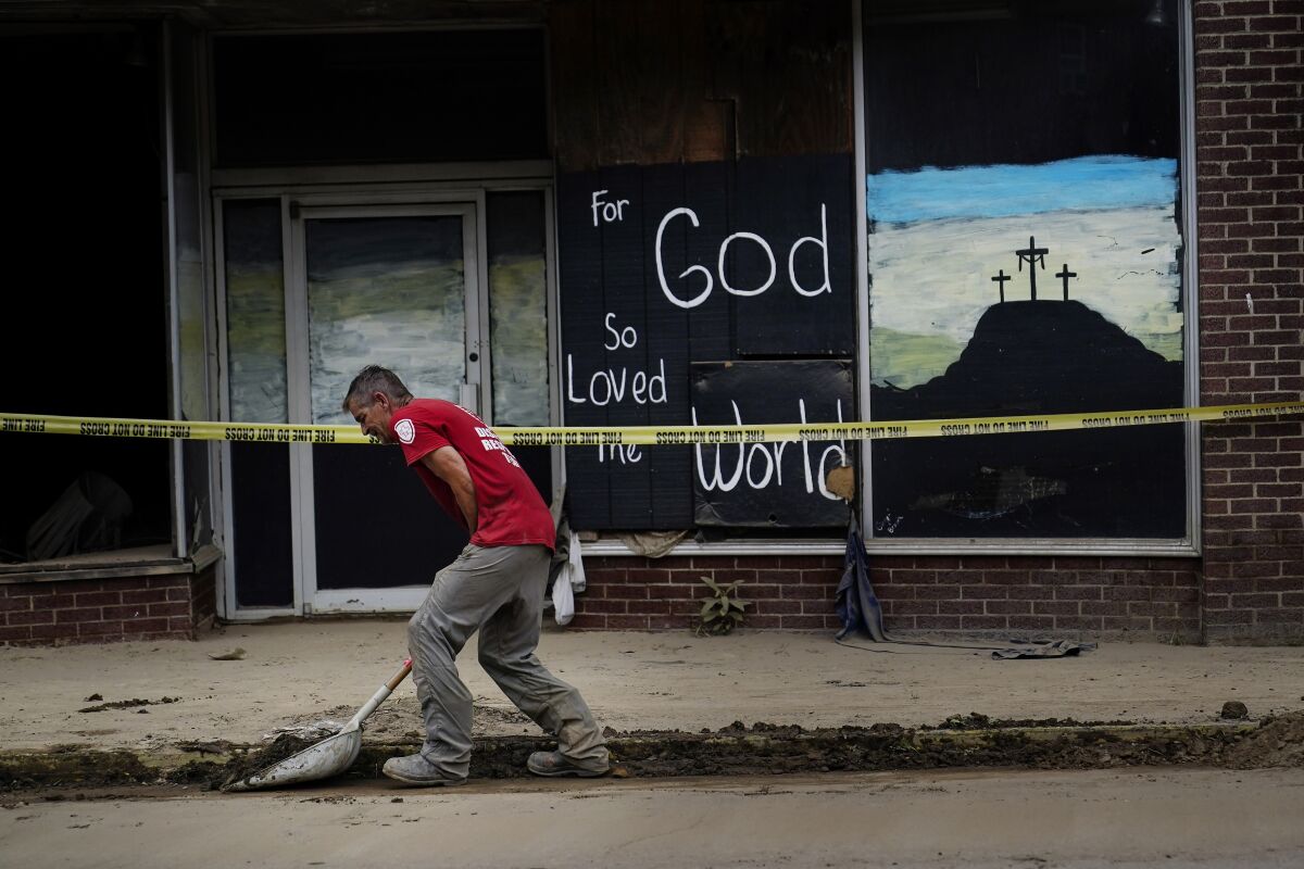 A volunteer shovels dirt and debris off of the main street in downtown Fleming-Neon, Ky., on Friday, Aug. 5, 2022. The previous week's massive flooding damaged much of the town. (AP Photo/Brynn Anderson)