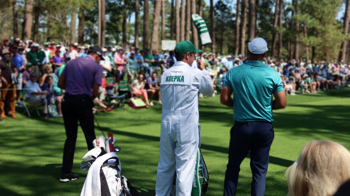 A professional golfer and his caddie stand, backs to the camera, on the golf course at the Masters Tournament