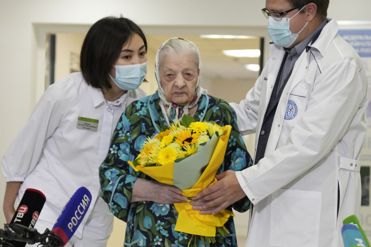 Dr. Vsevolod Belousov, right, and Dr. Saltanat Bekeeva, left, greet 101-year-old patient Pelageya Poyarkova with flowers as she leaves the recovery ward for COVID-19 patients at the Federal Center for Brain and Neurotechnology in Moscow, Russia, Friday, Dec. 3, 2021. Russia has reported more than 9.7 million confirmed cases of COVID-19 in the pandemic and more than 270 thousands deaths, which experts believe could be undercounts. (AP Photo/Pavel Golovkin)