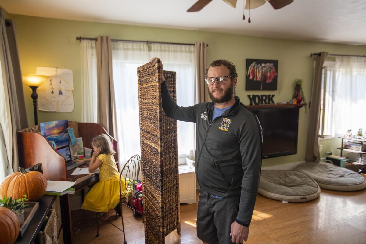 A man stands in his living room as his daughter sits at a desk