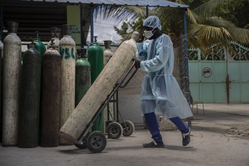 A hospital emplyee wearing protective gear as a precaution against the spread of the new coronavirus, transports oxygen tanks, in Port-au-Prince, Haiti, Saturday, June 5, 2021. Haiti defied predictions and perplexed health officials by avoiding a COVID-19 crisis for more than a year, but the country of more than 11 million people that has not received a single vaccine is now battling a spike in cases and deaths. (AP Photo/Joseph Odelyn)