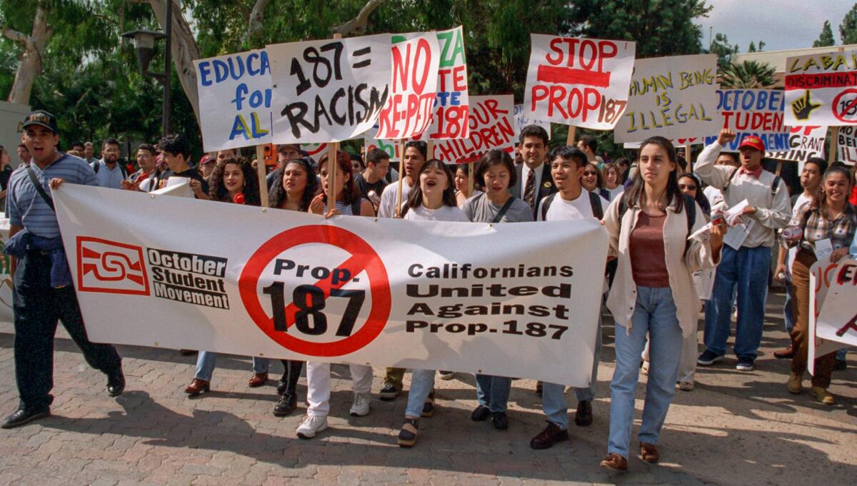 Protesters march with signs and banners with anti-Proposition 187 messages.