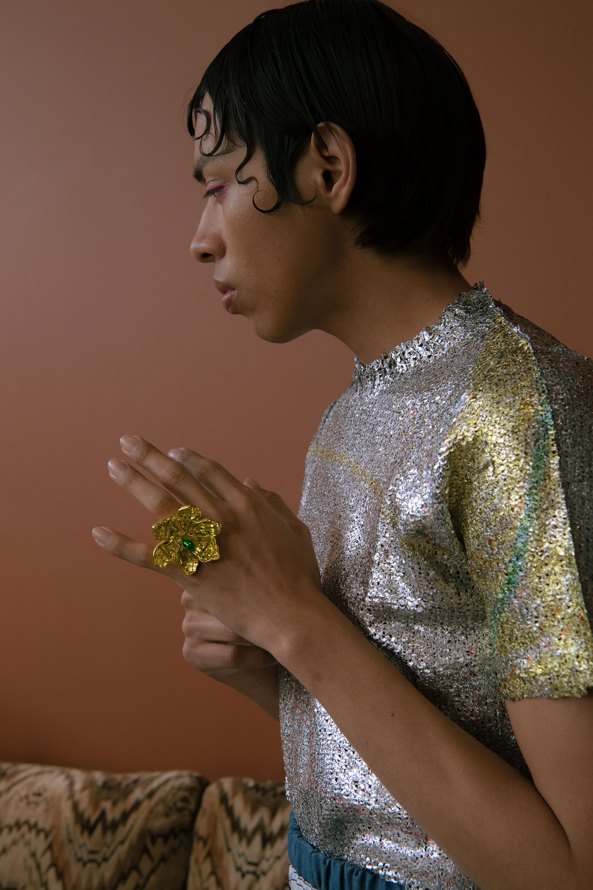 A closeup of a model in a silvery top wearing a flower-shaped ring.