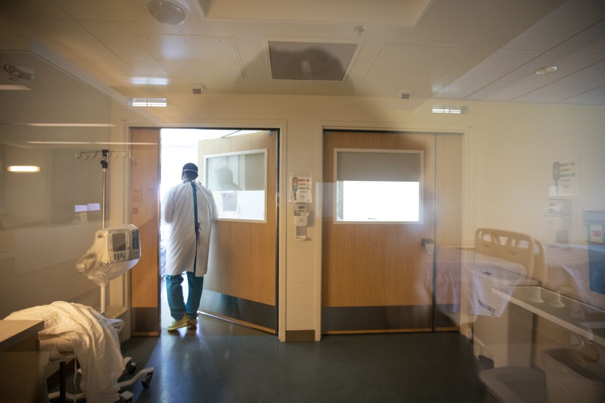 A patient care technician walks into an isolation room to check on a COVID-19 patient.