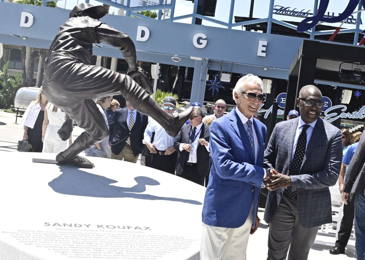 Sandy Koufax, left, shakes hands with the sculptor of his statue, Brandly Cadet, as the Los Angeles Dodgers unveil the statue in the Centerfield Plaza to honor the Hall of Famer and three-time Cy Young Award winner prior to a baseball game between the Cleveland Guardians and the Dodgers at Dodger Stadium in Los Angeles, Saturday, June 18, 2022. (Keith Birmingham/The Orange County Register via AP)
