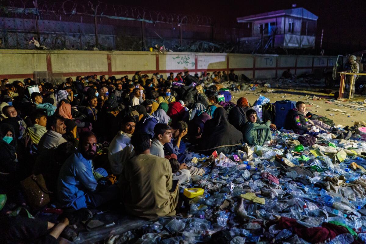 Afghan refugees crouch together as a soldier stands by