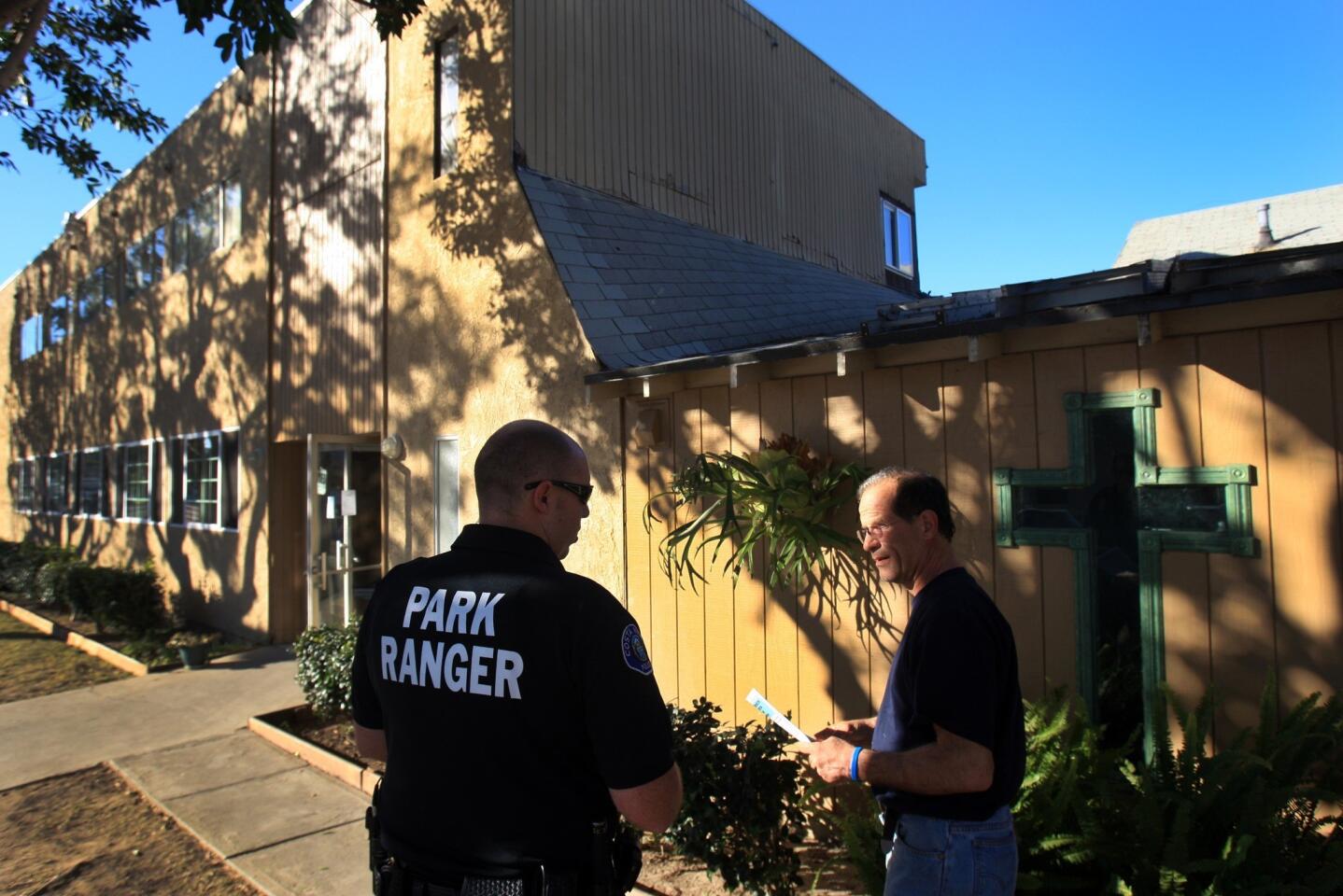 Costa Mesa Park Ranger M. Pallo greets and hands out a flier to Peter K., who is formerly homeless and now works and lives at the Lighthouse Outreach Church in Costa Mesa.