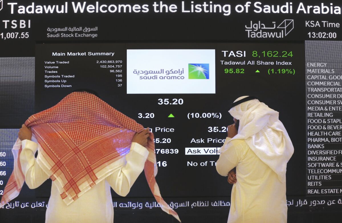 FILE - In this Dec. 11, 2019, file photo, Saudi stock market officials watch the stock market screen displaying Saudi Arabia's state-owned oil company Aramco after the debut of Aramco's initial public offering on the Riyadh's stock market in Riyadh, Saudi Arabia. Saudi Arabia's oil company Aramco reached a $2 trillion valuation as it hit near record levels on Wednesday, Oct. 6, 2021, during trading hours. (AP Photo/Amr Nabil, File)