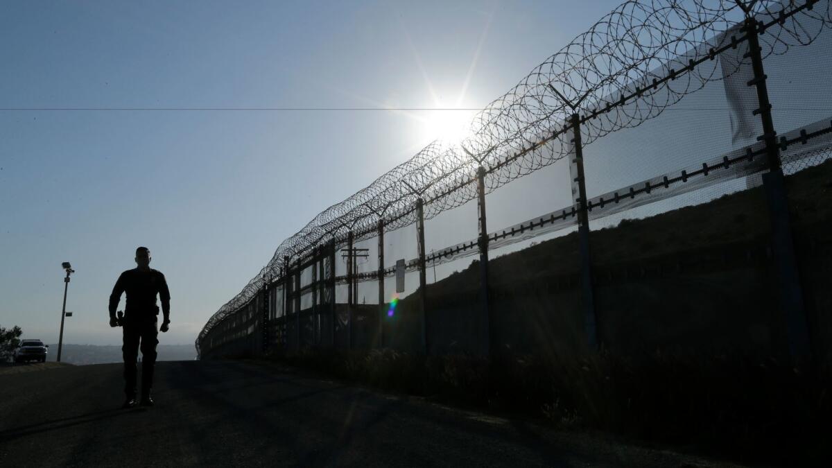 A Border Patrol agent walks along the border in San Diego County, Calif., in June.