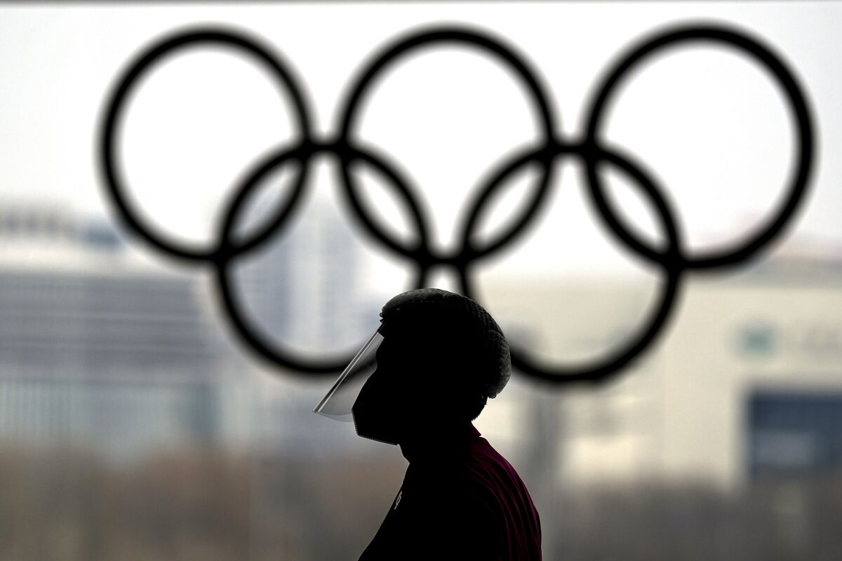 A person wearing a face shield walks past the Olympic rings inside the main media center at the 2022 Winter Olympics, Wednesday, Jan. 19, 2022, in Beijing. (AP Photo/David J. Phillip)