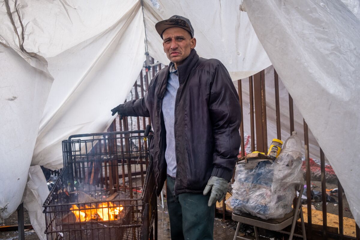 Carlos Parra Aguiar stands next to a grocery cart fire he built to stay warm. 