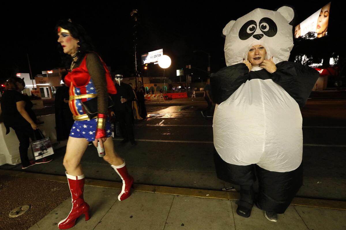Kathryn Anderson dresses as a panda while "Wonder Woman" walks by at the Halloween Carnaval.