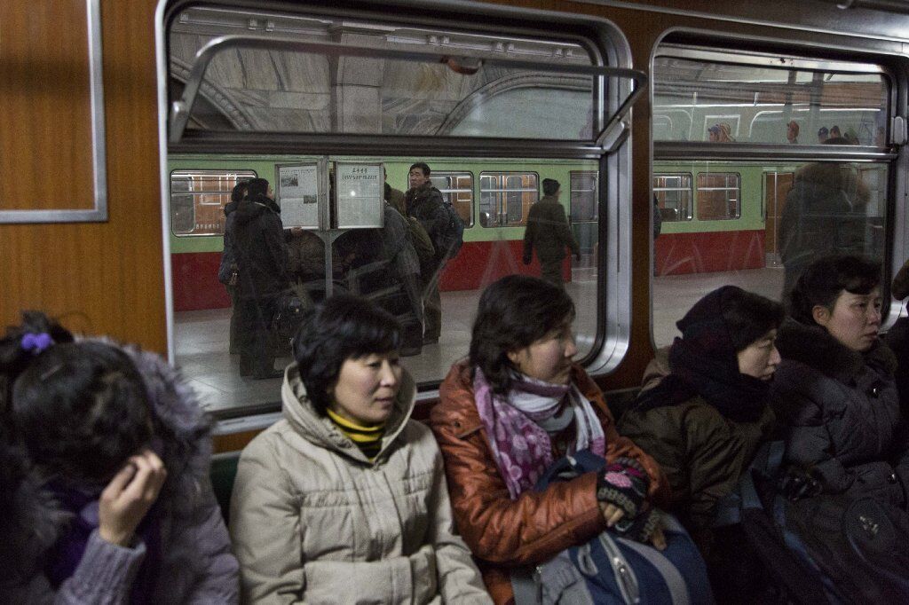 North Koreans ride the subway as other commuters, behind them on the train platform, gather around a public newspaper stand in Pyongyang to read the headlines about executed leader Jang Song Taek.