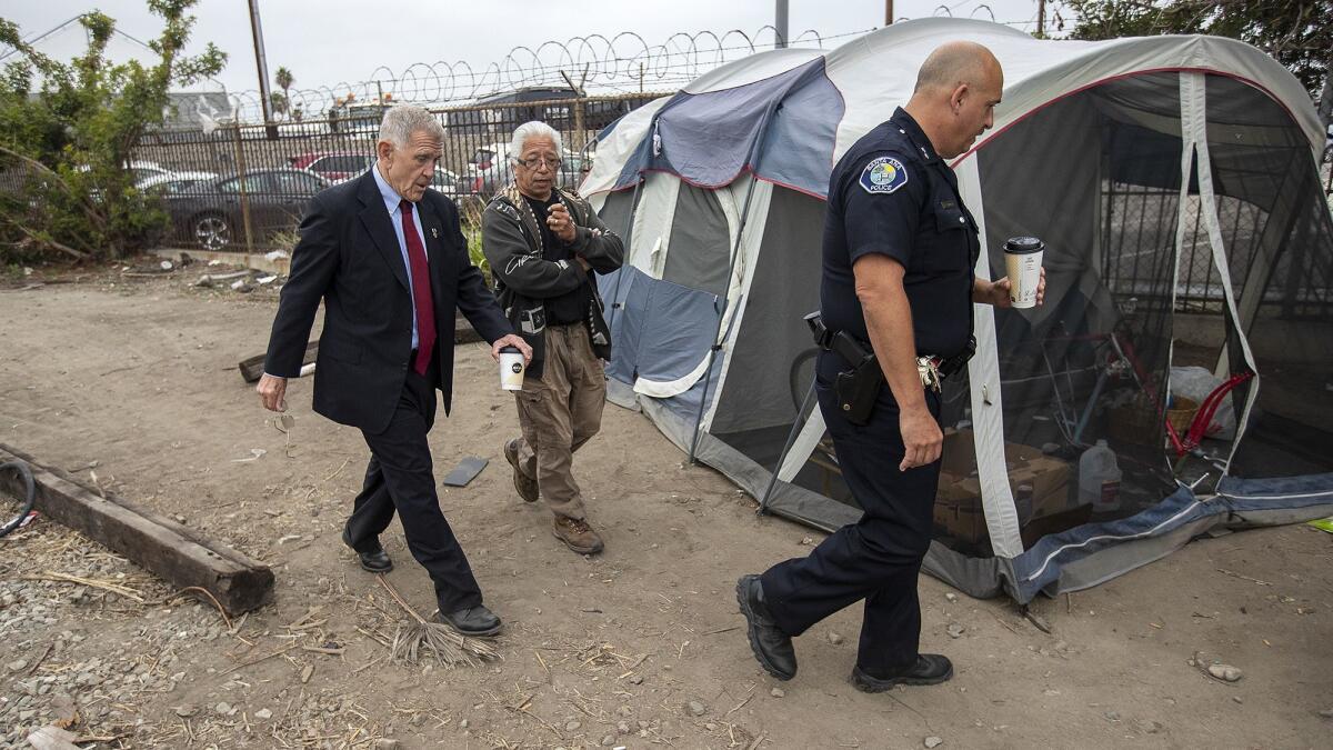 U.S. District Judge David Carter, left, homeless activist Lou Noble and Deputy Chief Ken Gominsky of the Santa Ana Police Department walk past a tent along railroad tracks near Main Street in Santa Ana.